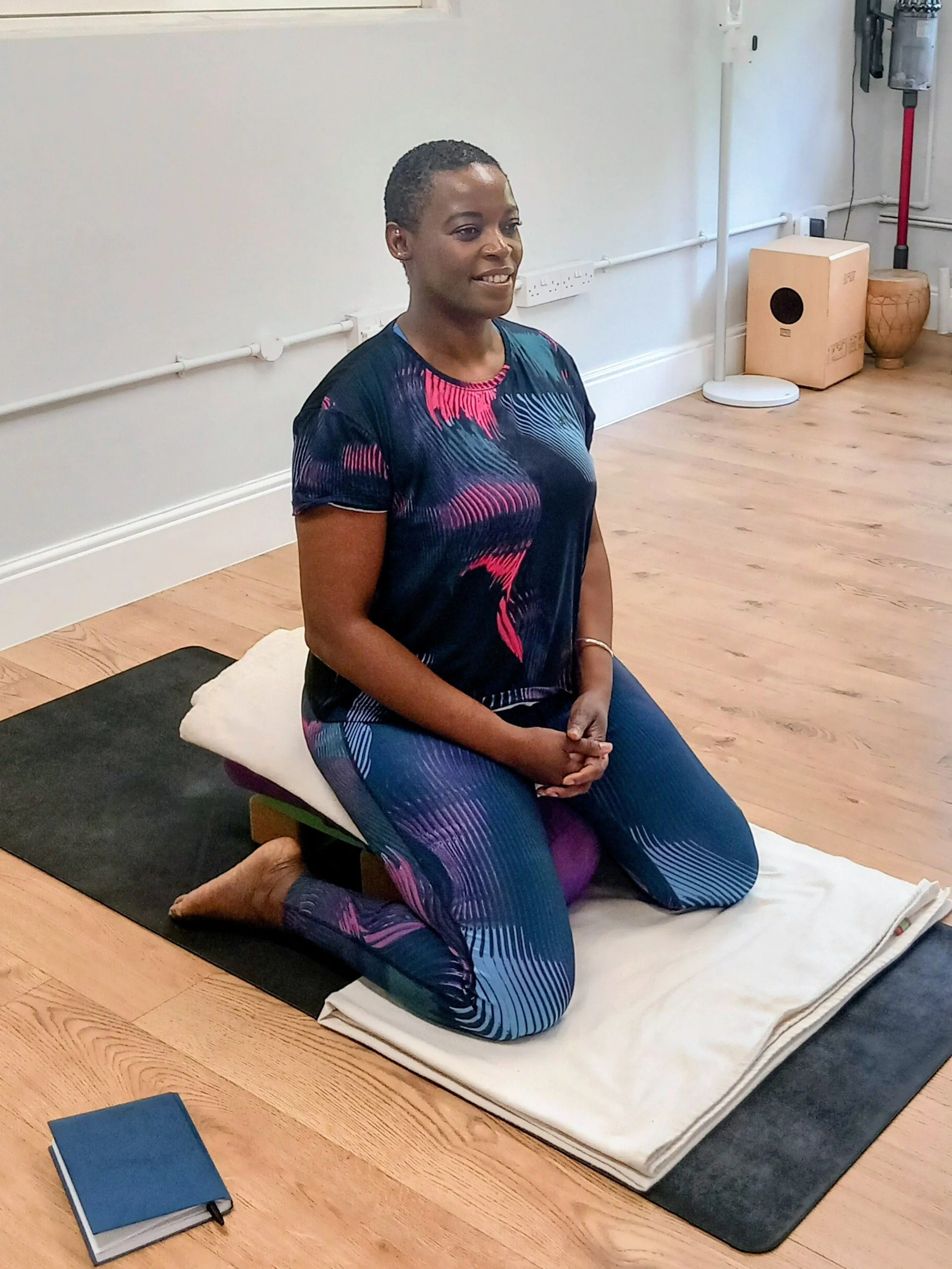 A woman practicing a seated position on a meditation cushion in a yoga studio.