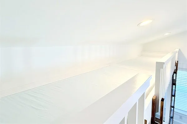 A white loft bed with a mattress, built-in shelves, and slanted ceiling with small windows.