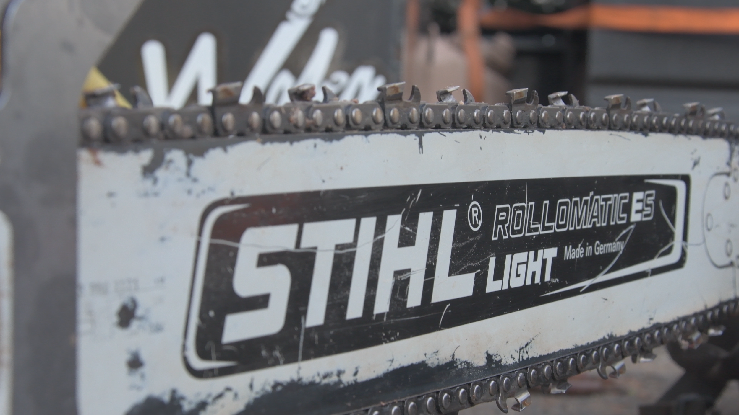 Close-up of a chainsaw chain bar with the brand name 'Stihl Light Rollomatic ES' and marks of wear and scratches.