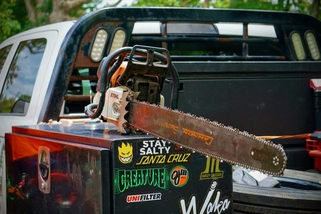 A chainsaw resting in the back of a pickup truck with outdoor background.