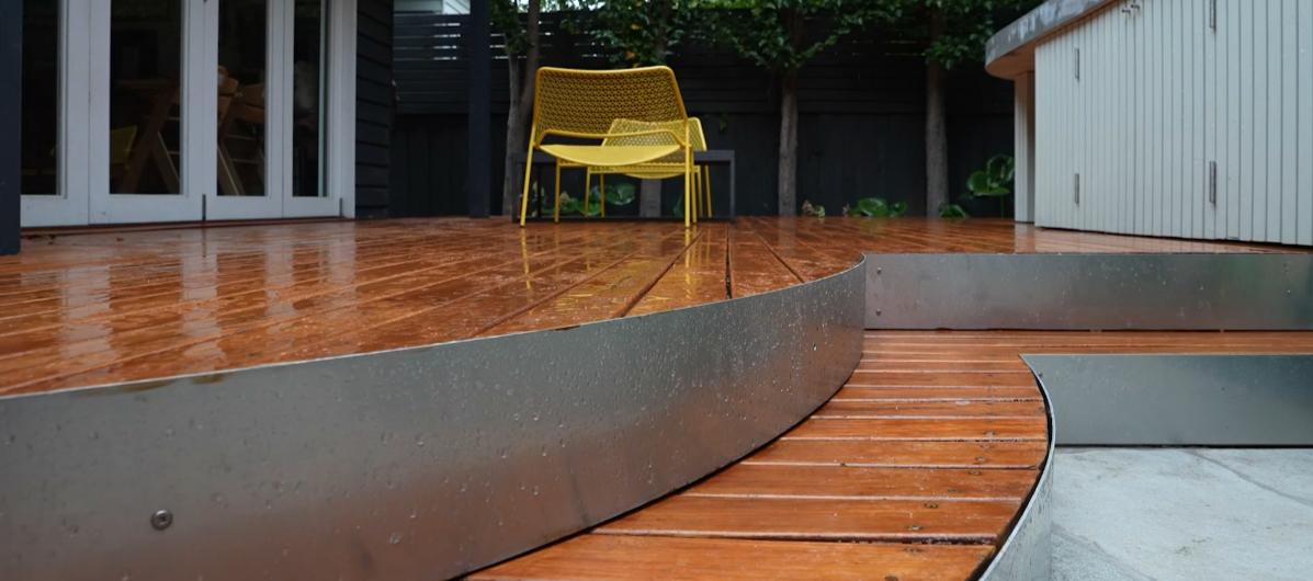 Rain-soaked wooden deck with yellow chairs and a glass door leading inside a house.