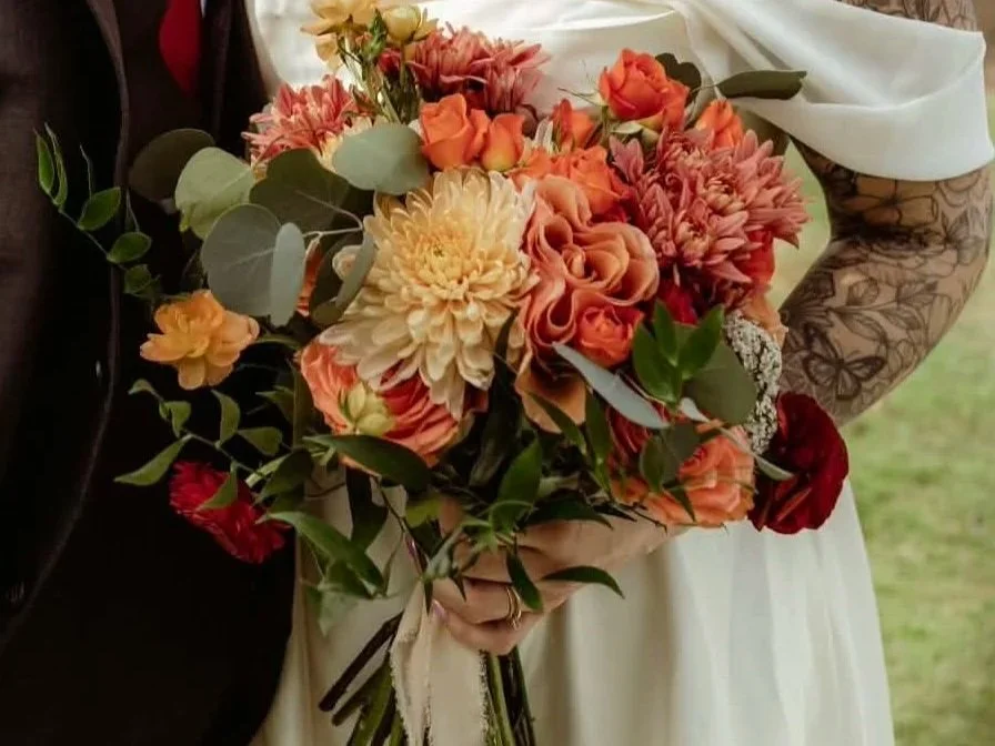A woman holding a bouquet of peach and cream-colored flowers, including dahlias and roses, with green foliage and some red accents.