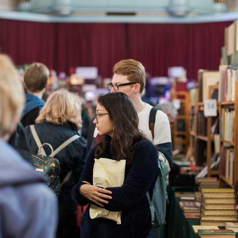 Crowded book fair with people browsing shelves.