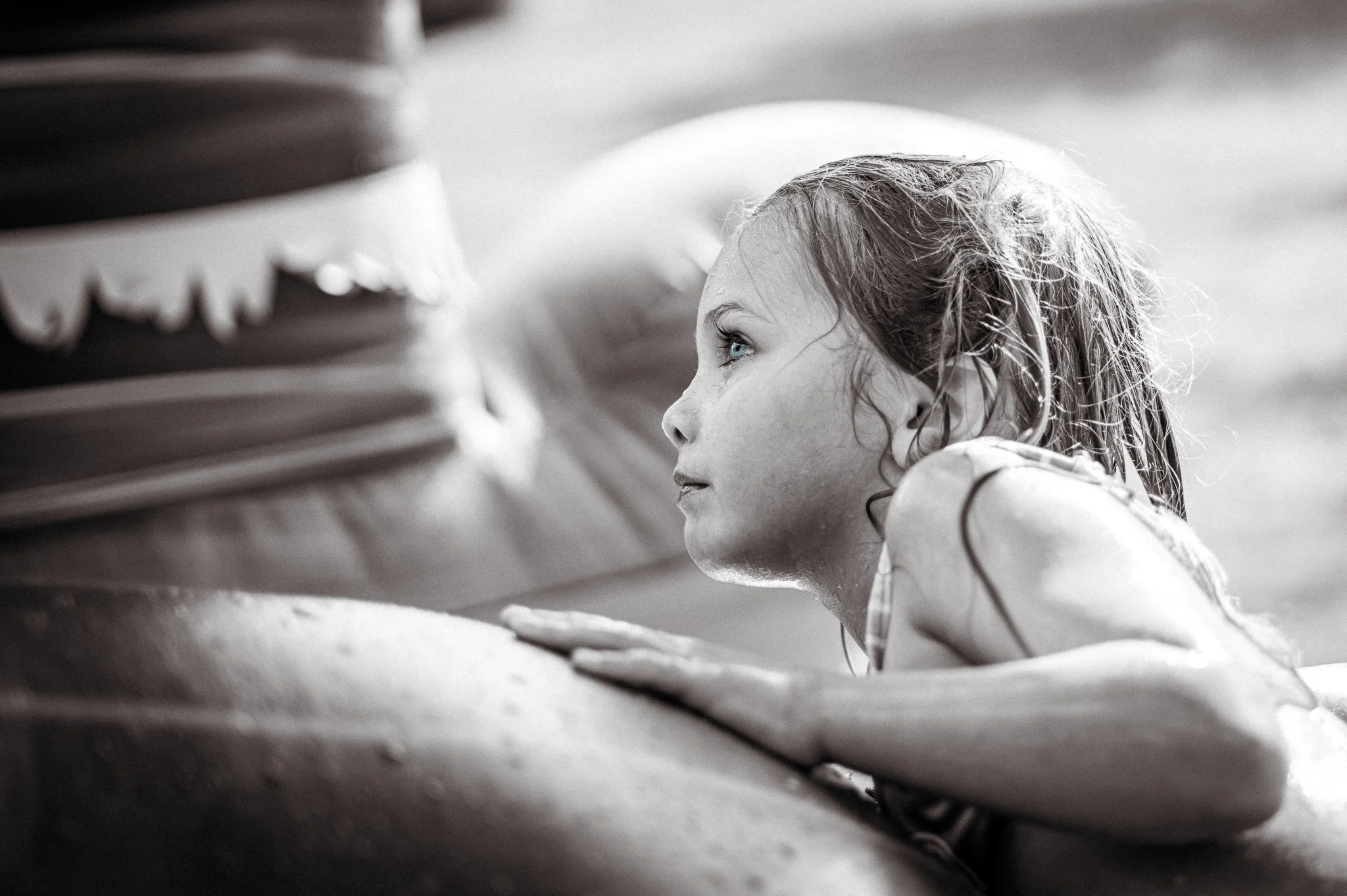 Young girl lying face down on the ground, looking intently at something in front of her. Black and white photo.