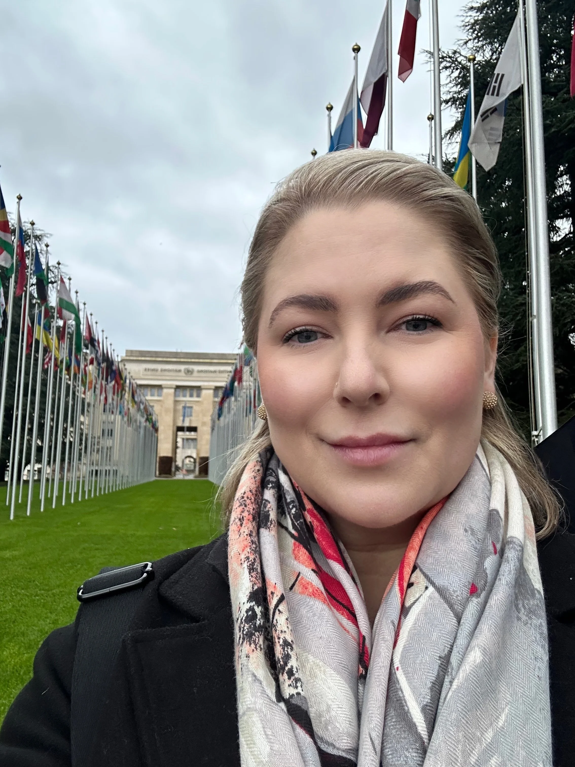 A woman taking a selfie in front of numerous flags and a large building.