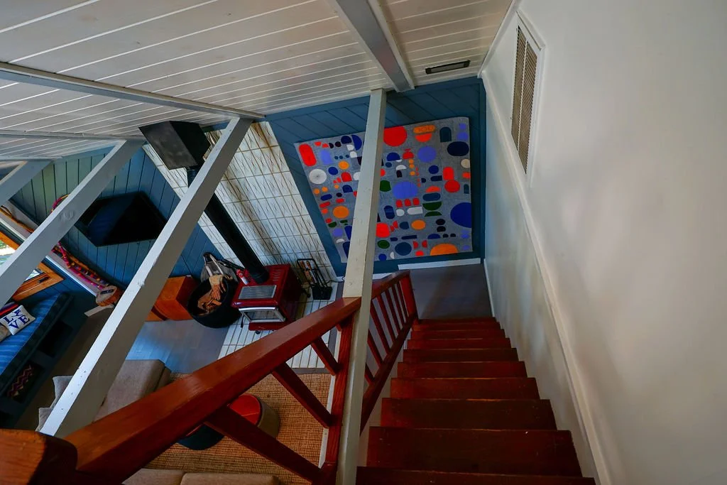Wood stairs leading down from a loft into a living area with blue walls, a white slanted ceiling, and an open cabin-style design.