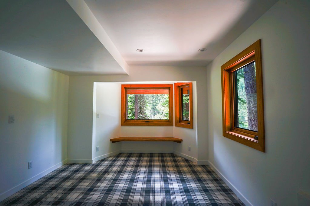 Bright white room with blue and white plaid carpeting, multiple windows with natural wood frames, and a built-in bench beneath the windows.