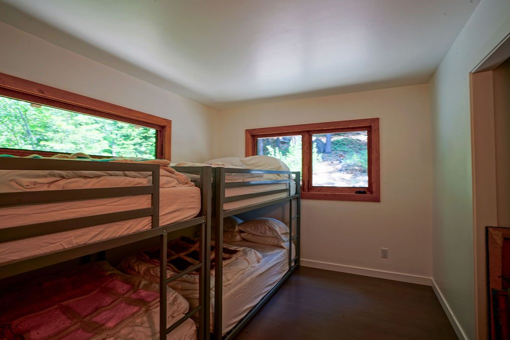 Bunk room with two side-by-side bunk beds, white walls, dark wood flooring, and narrow windows above the bunks and at the end of the room.