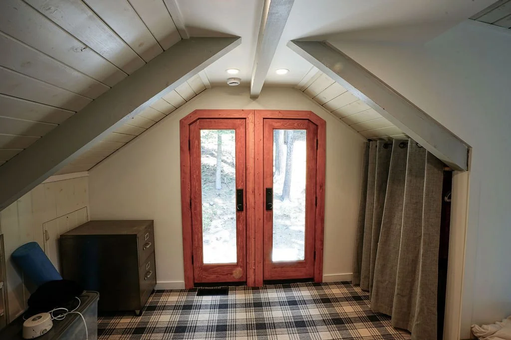 Room with double wood doors featuring glass panels, a peaked white wood-paneled ceiling, and blue and white plaid carpet.