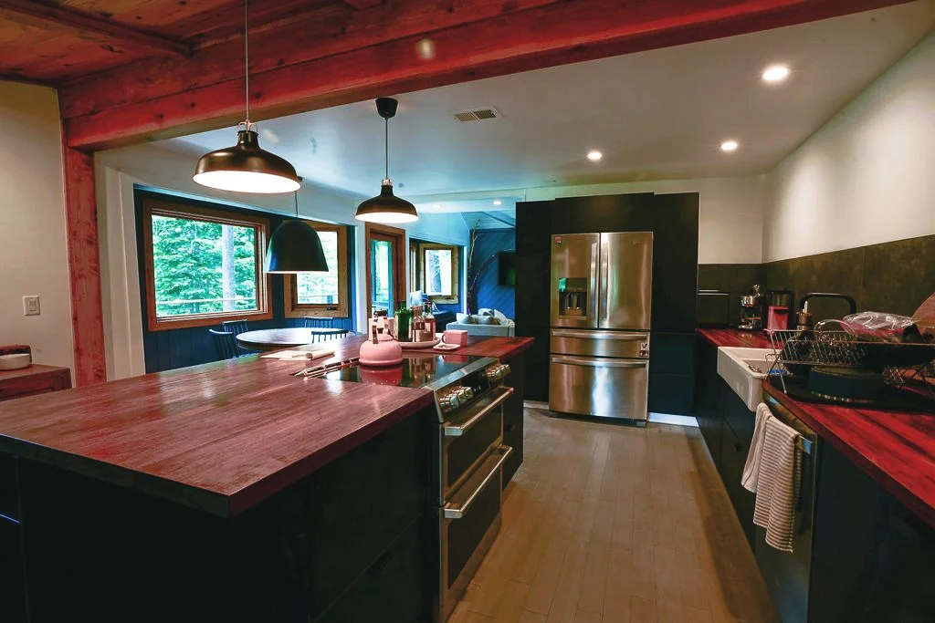 Kitchen with exposed wood beams, wood countertops, dark cabinetry, a stainless steel refrigerator, and a white farmhouse sink.