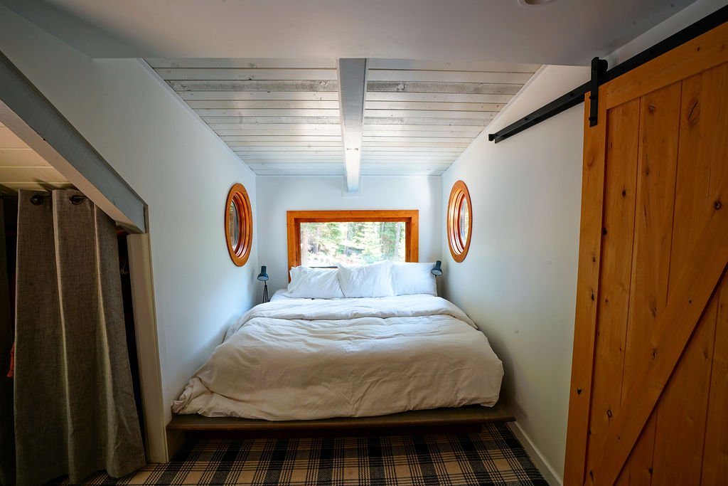 Cozy bedroom nook with a bed beneath a rectangular window and two small circular windows on either side.