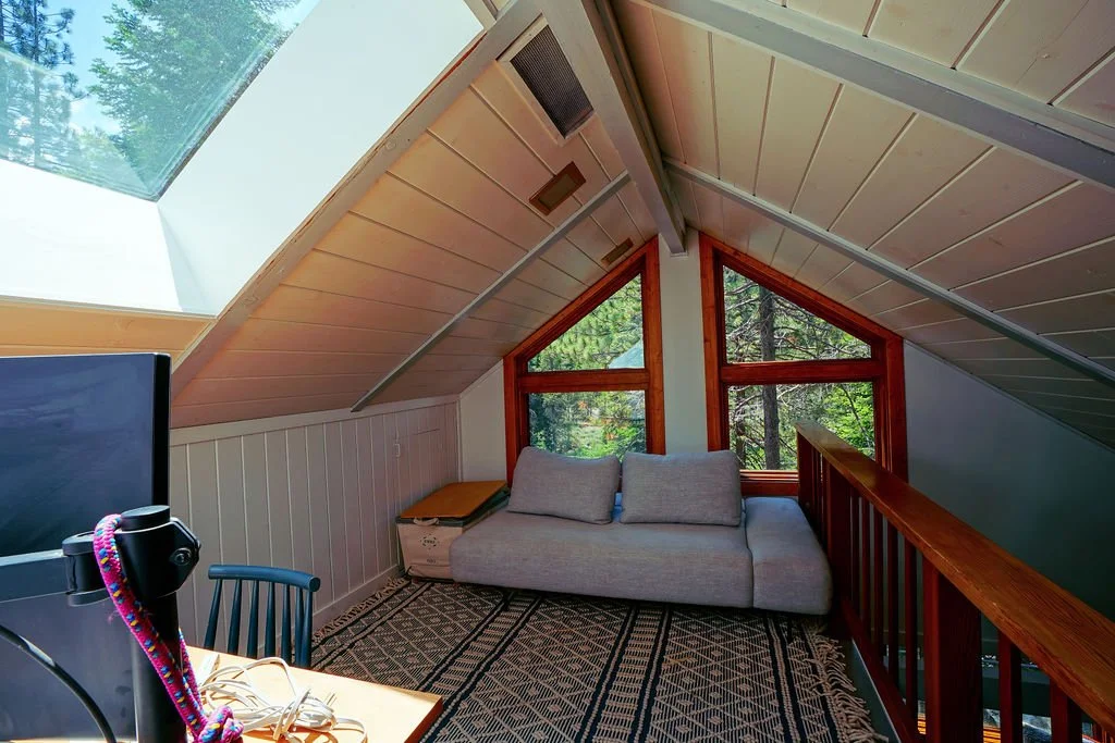 Bright loft with a blue patterned rug, wooden railing, skylight, white ceiling, and triangular windows.
