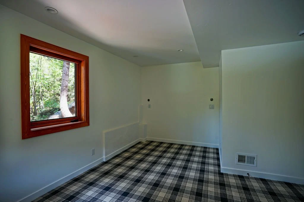 Bright white room with blue and white plaid carpeting and a window featuring a natural wood frame.