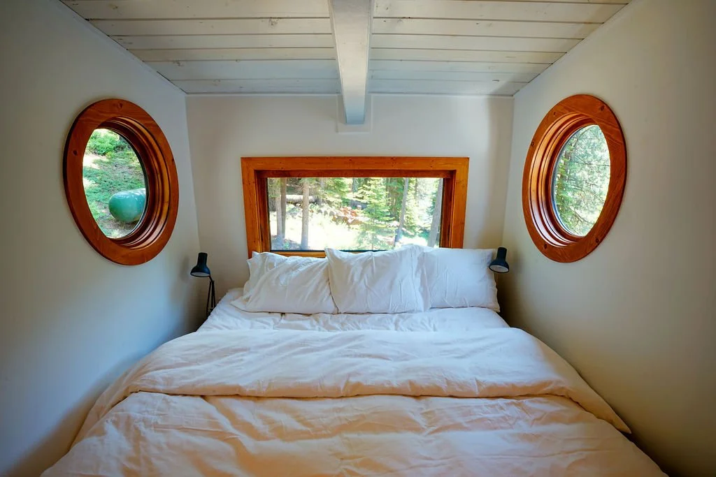 Cozy bedroom nook with a bed beneath a rectangular window and two small circular windows on either side.