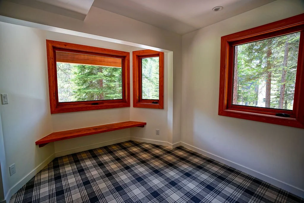 Bright white room with blue and white plaid carpeting, multiple windows with natural wood frames, and a built-in bench beneath the windows.