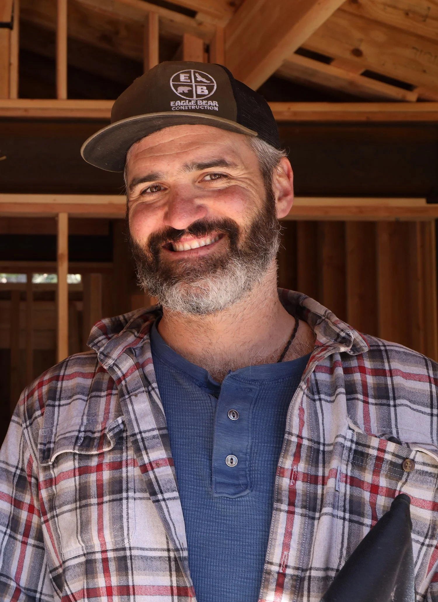 steven kirk owner of eagle bear construction stands in framed new construction wearing a company hat and flannel shirt