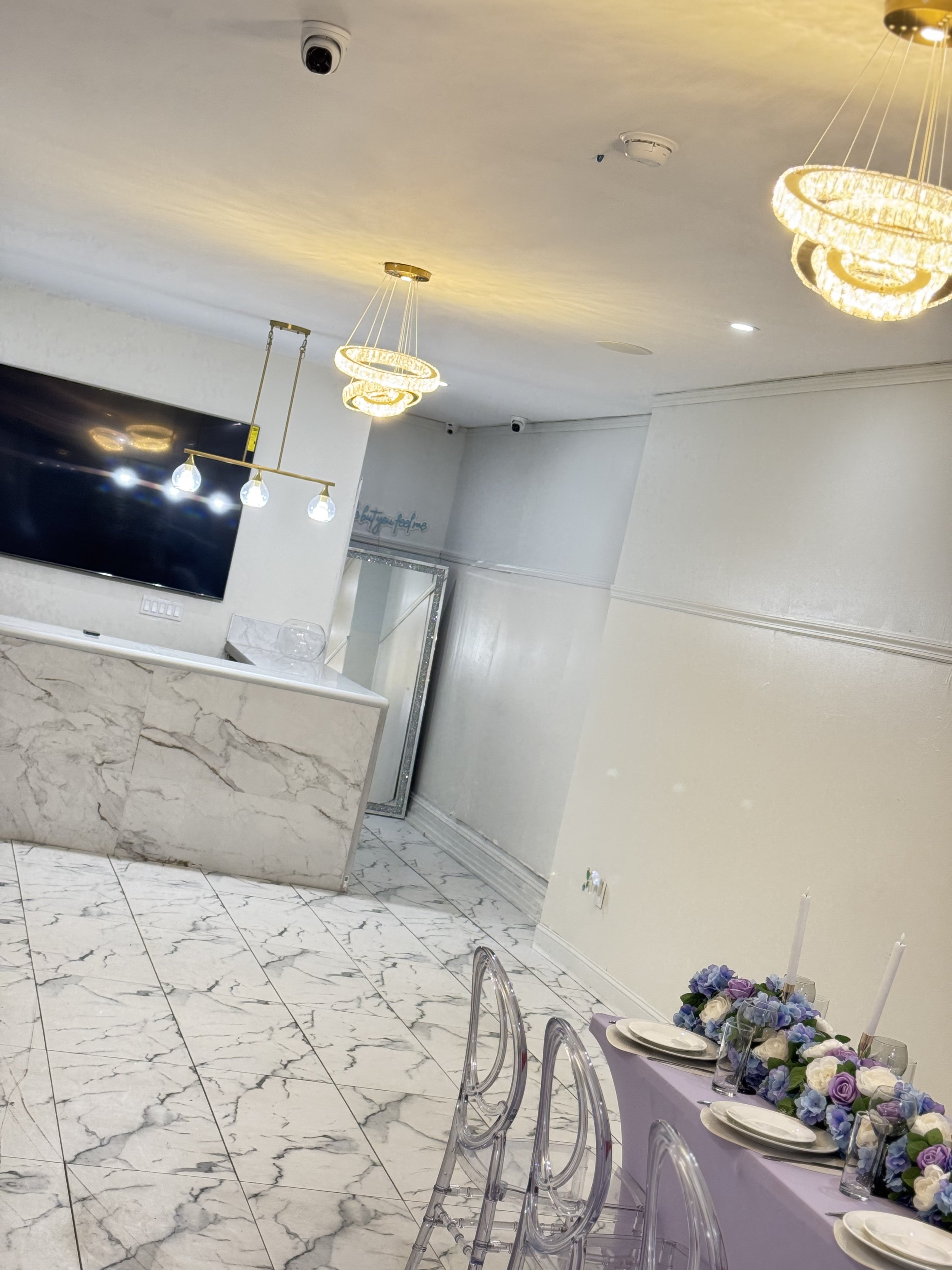 Elegant interior with marble flooring, transparent chairs, a decorated table with flowers, and modern chandeliers.