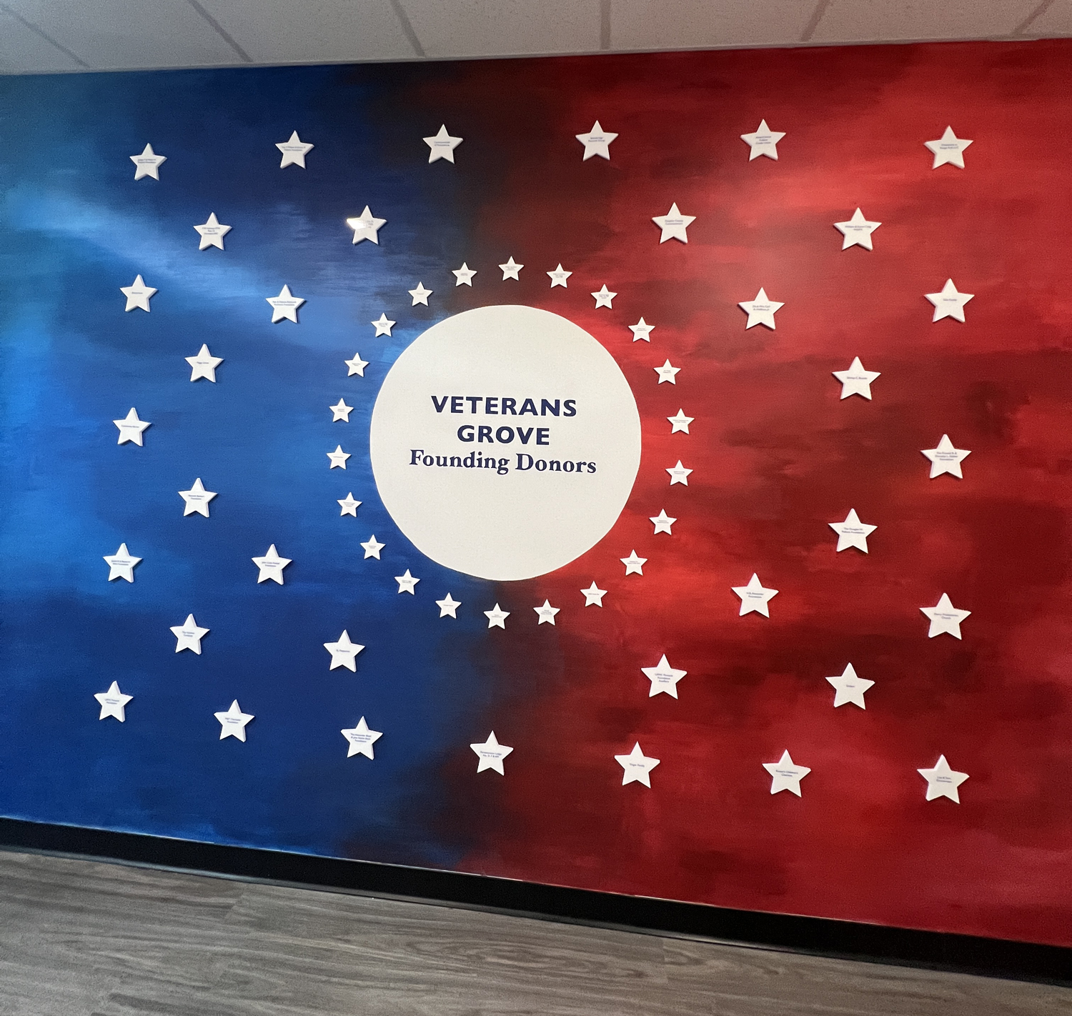 Wall display with red, white, and blue background featuring white star cutouts, centered around a white circle with the text 'VETERANS GROVE Founding Donors'.