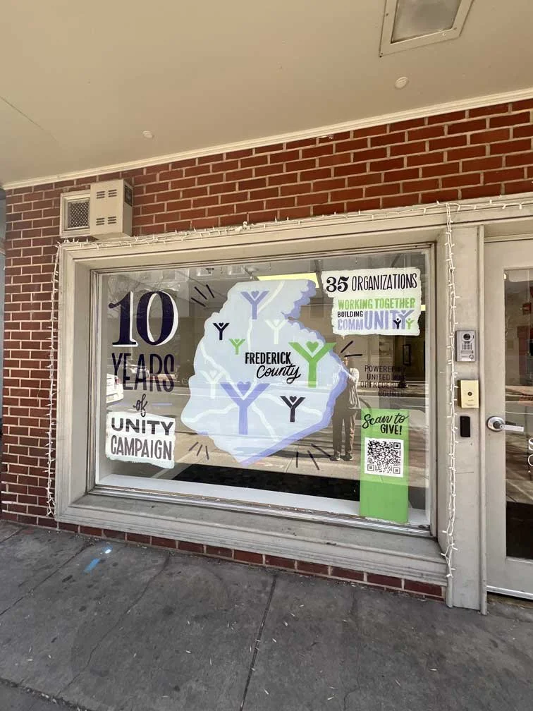 Decorative window display celebrating 10 years of a unity campaign for Frederick County, featuring a map outline, trees with people, and text about organizations working together for community.