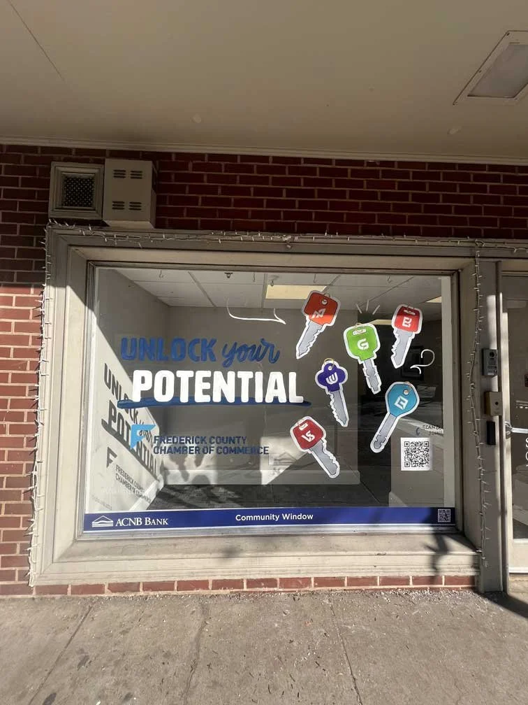 Decorated community window with signs that say 'UNLOCK your POTENTIAL' and images of colorful keys with different letters, promoting a message from the Frederick County Chamber of Commerce and ACNB Bank.
