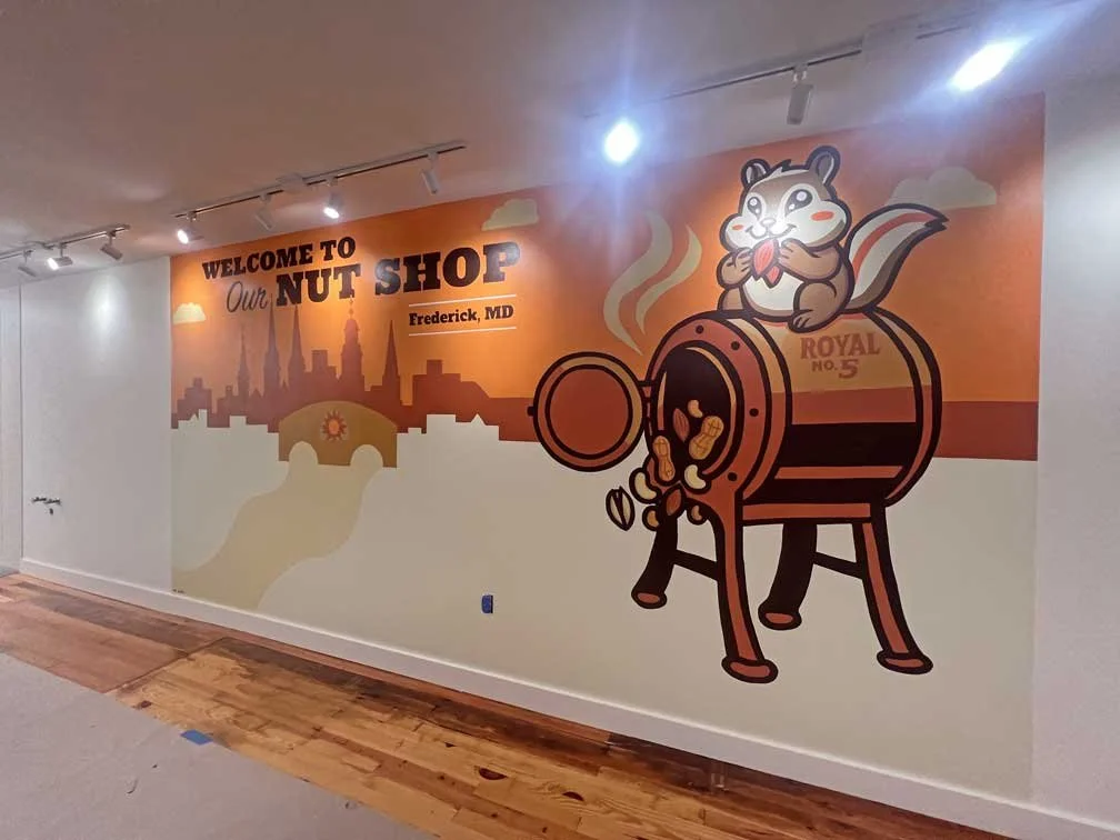Colorful wall mural welcoming visitors to a nut shop in Frederick, Maryland, featuring a cartoon squirrel eating a nut and a coffee roaster with steaming coffee beans.