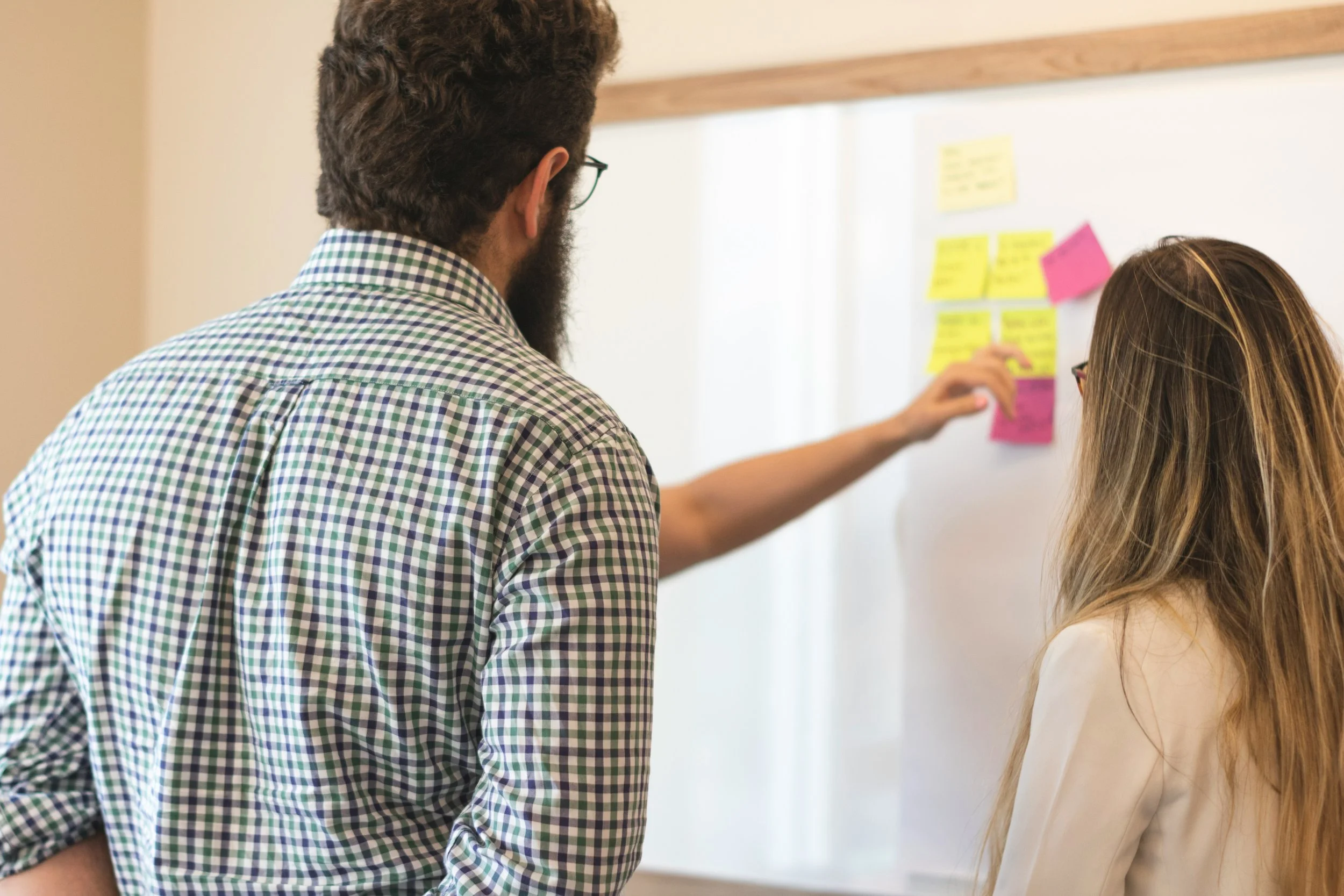 Two people discussing content on a whiteboard with colorful sticky notes.