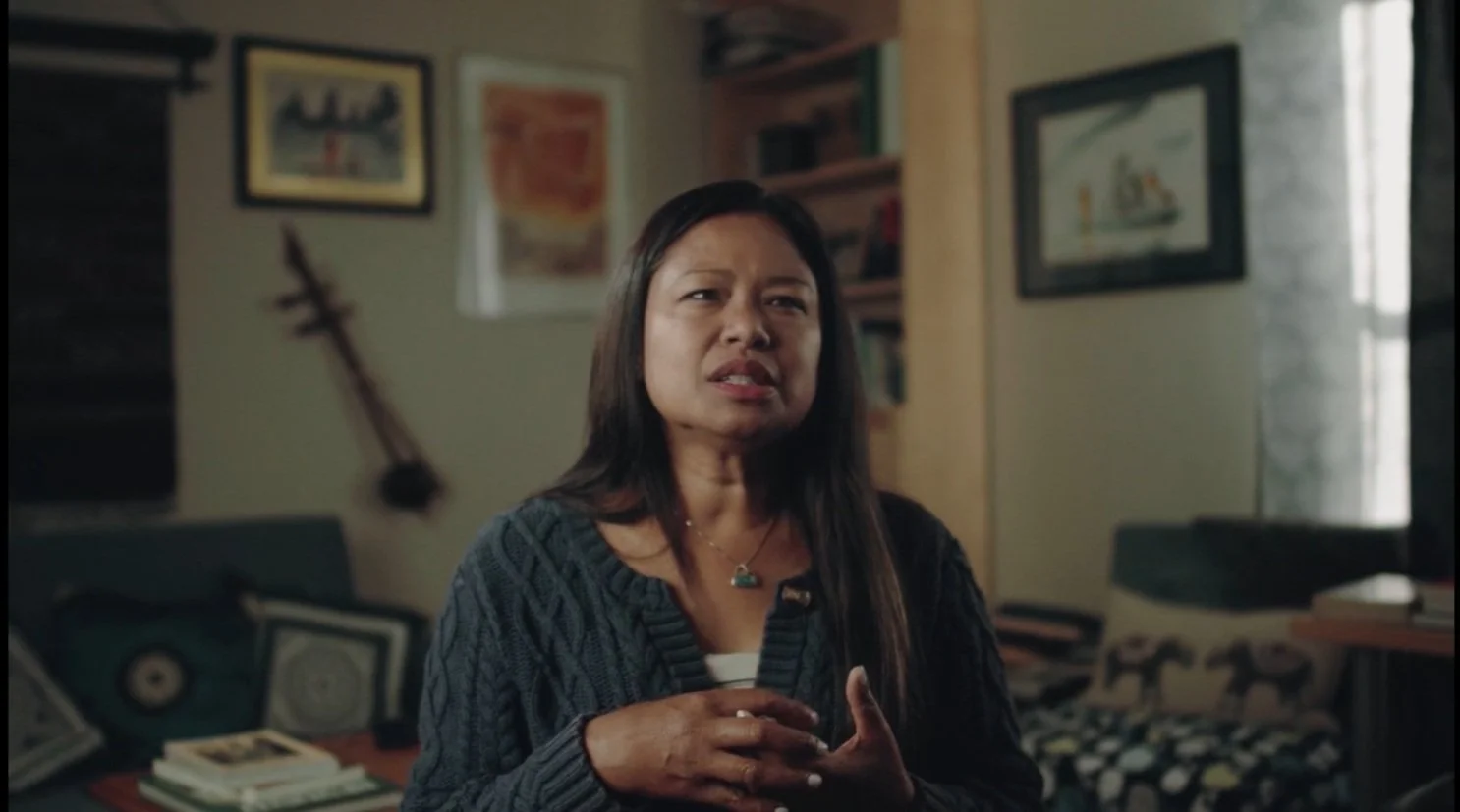 Person speaking in a cozy room with wall art and books