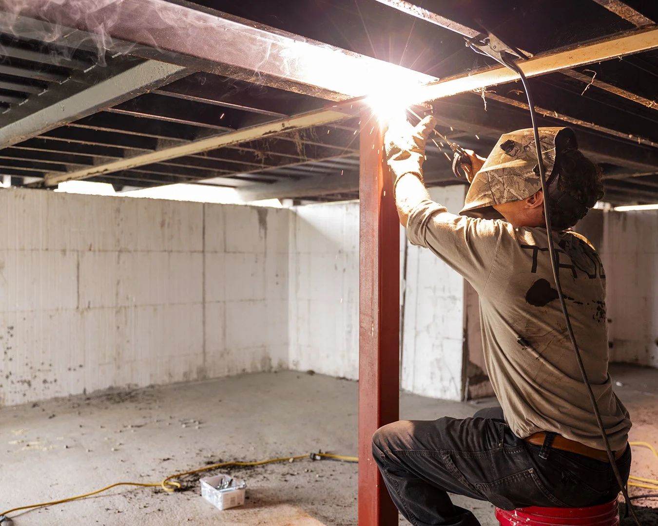 Welder securing support beams under container home