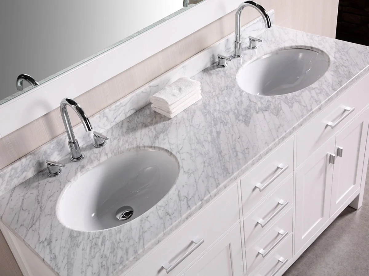 Double bathroom vanity with marble countertop, two oval sinks, two chrome faucets, and a stack of folded white towels.