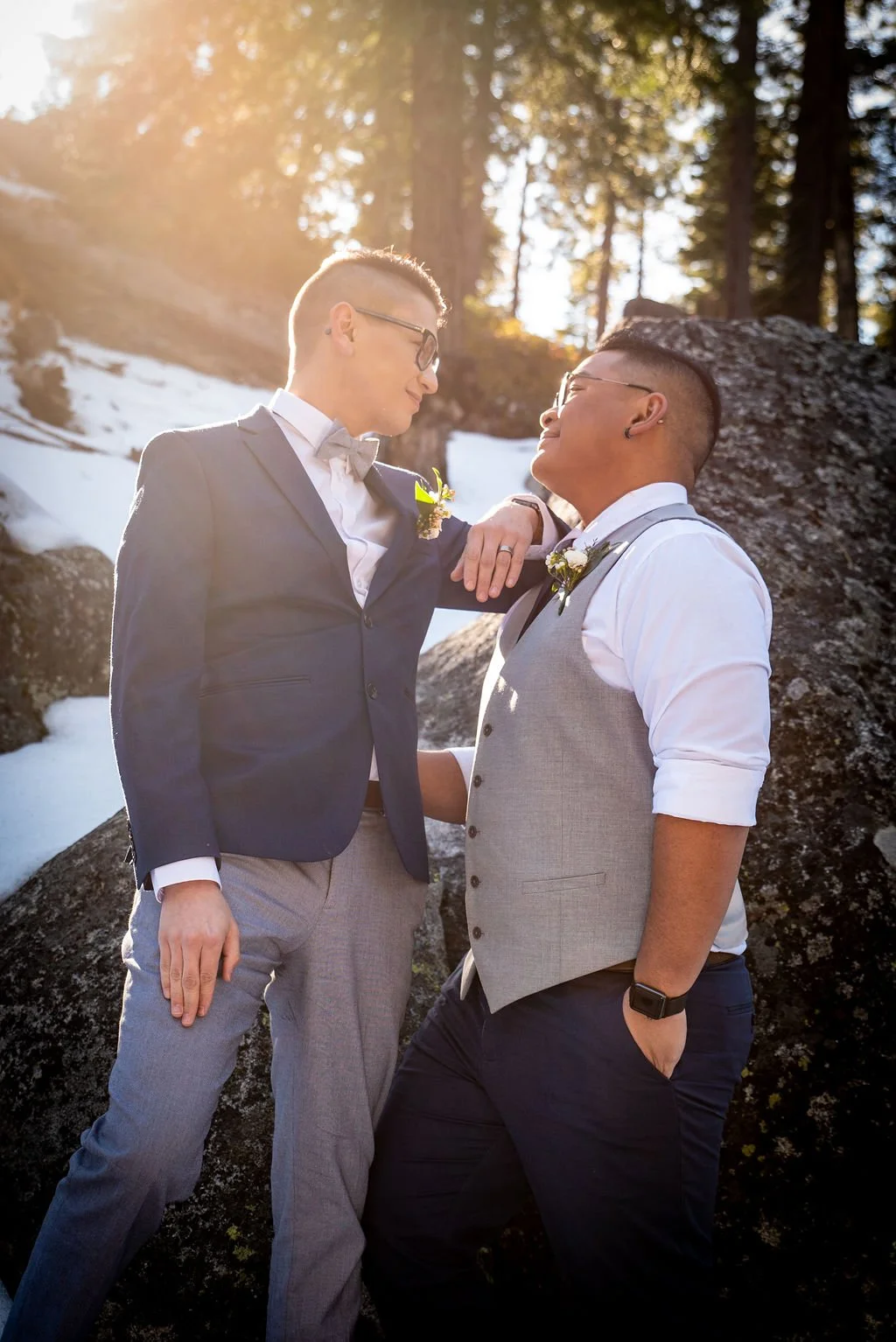 Two gay men in wedding attire, one in a navy blazer and grey pants, sharing an intimate moment outdoors in snowy tahoe