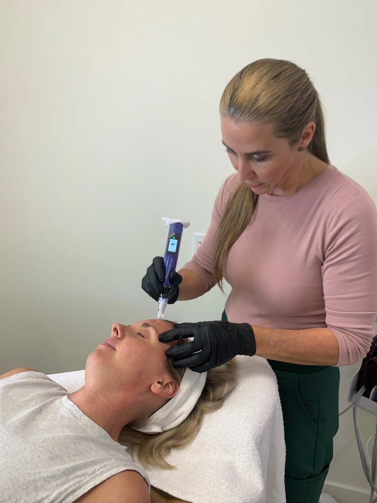 A woman receiving a facial treatment with a syringe-like device from a professional in a clinical setting.