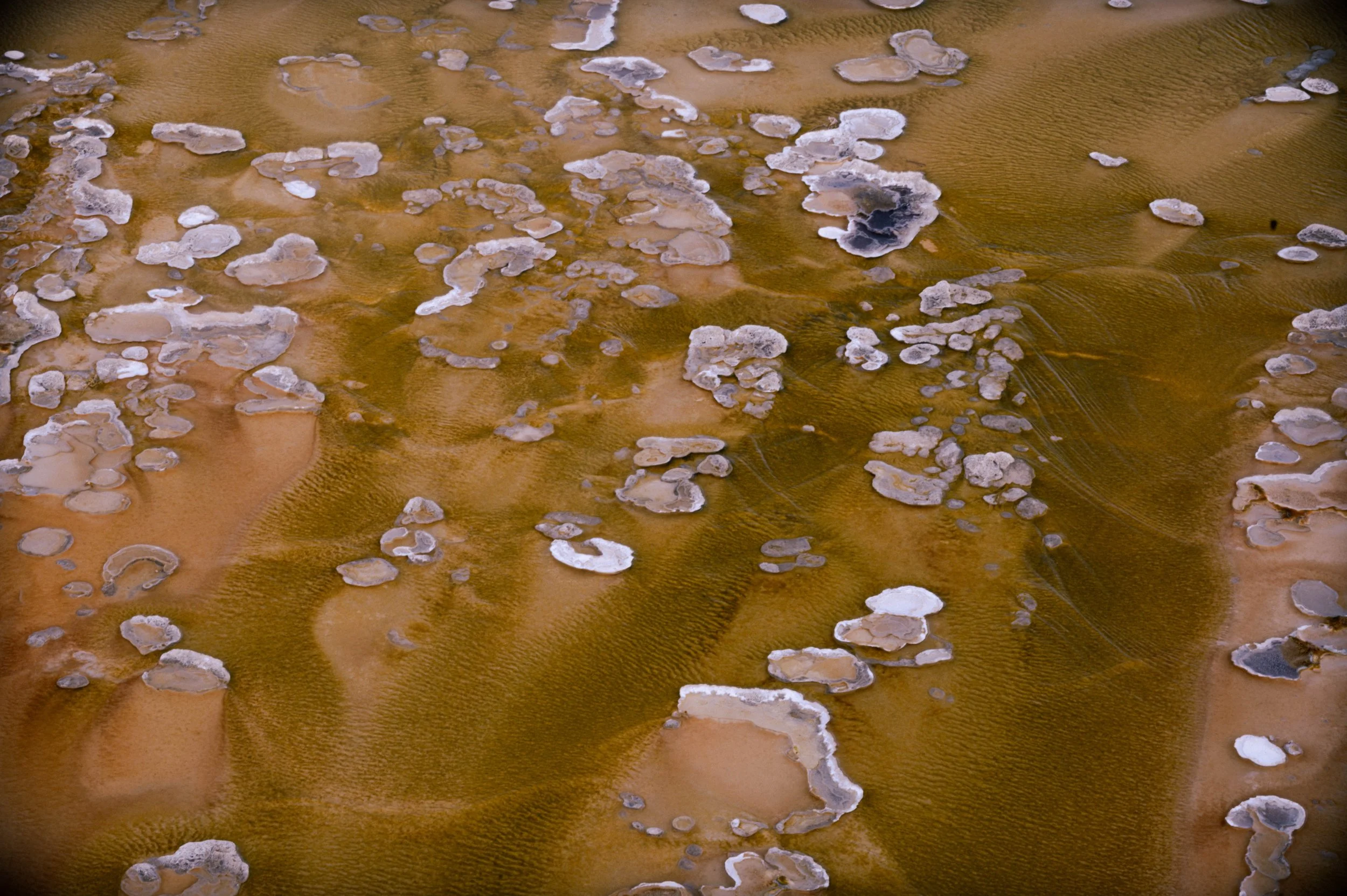 Close-up aerial view of rocks and salt formations on a brown, desert-like landscape.