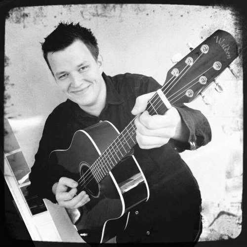 Portrett av Inge Åsen – trubadur fra Trondheim med gitar, kjent for festmusikk og engasjerende liveopptredener.
