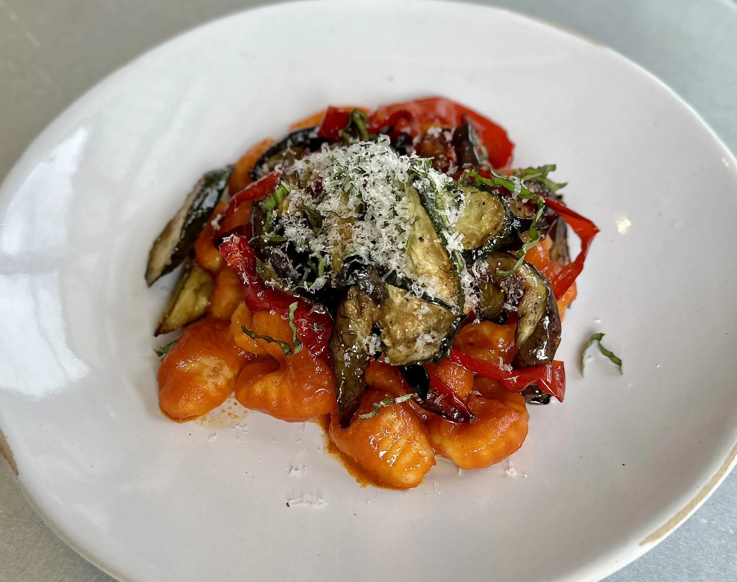 A plate of gnocchi topped with roasted vegetables, shredded cheese, and chopped herbs.
