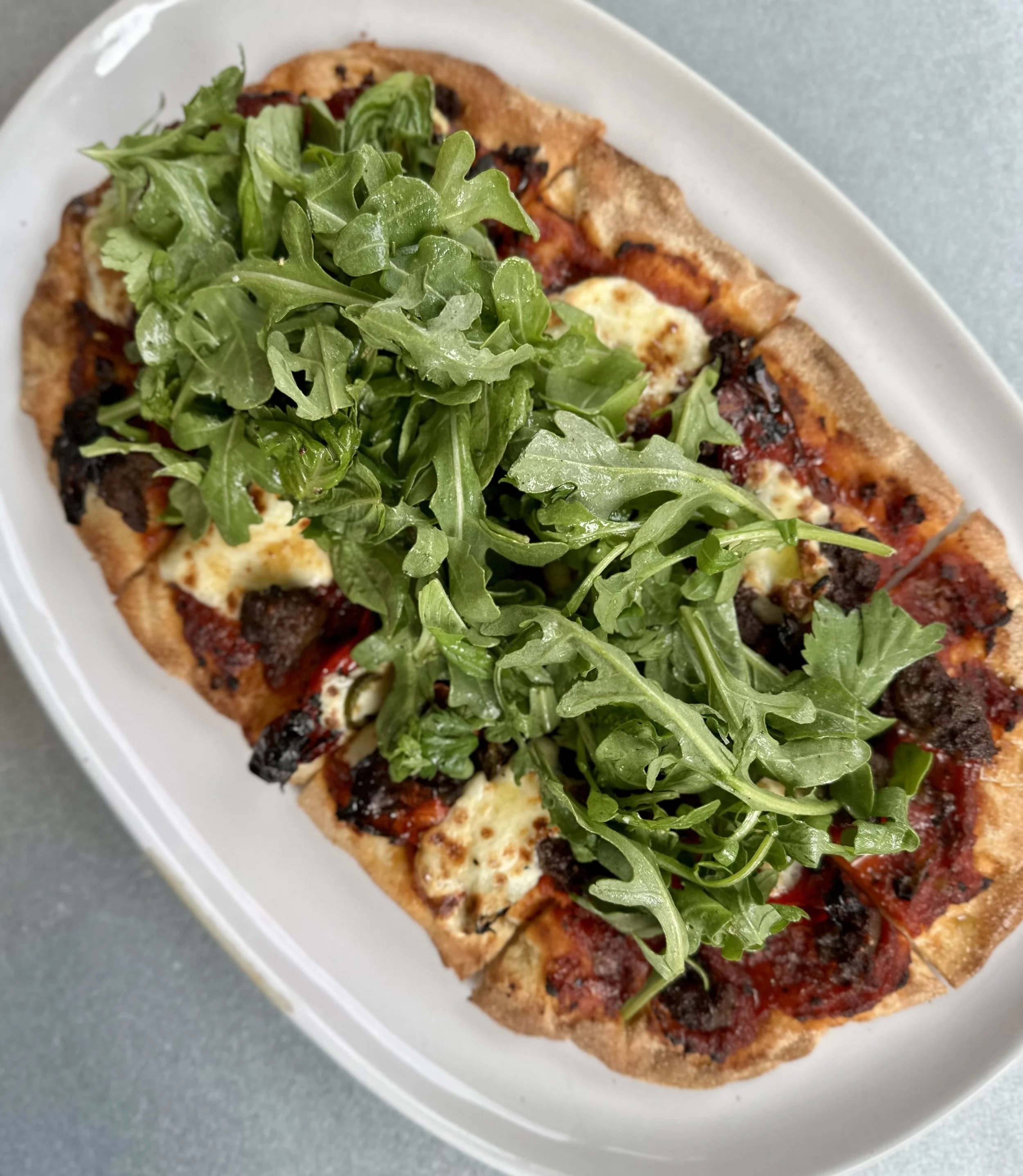 Slice of pizza topped with arugula leaves on a white oval dish.