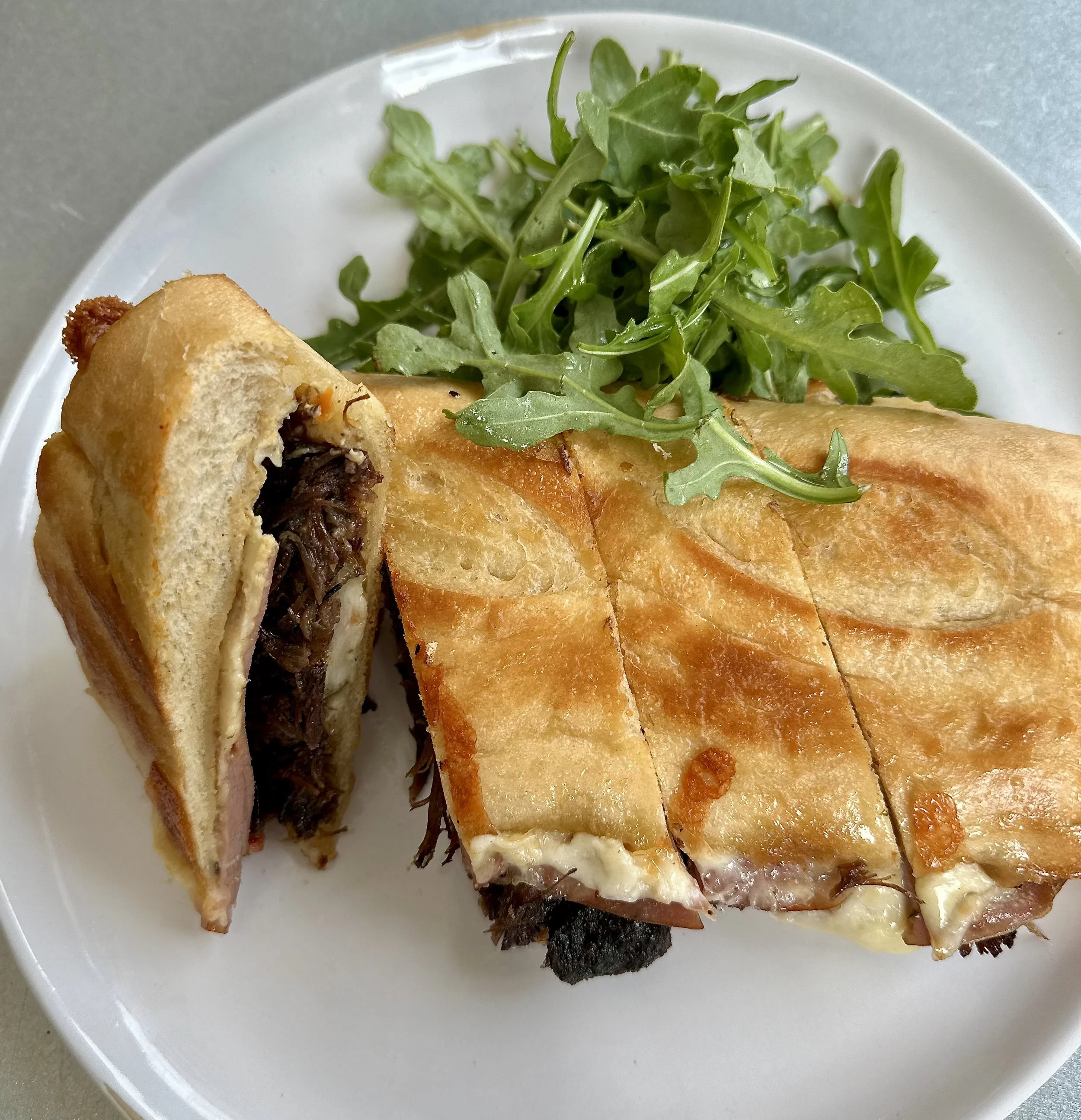 Sandwich with shredded beef and melted cheese, served with a side of arugula on a white plate.