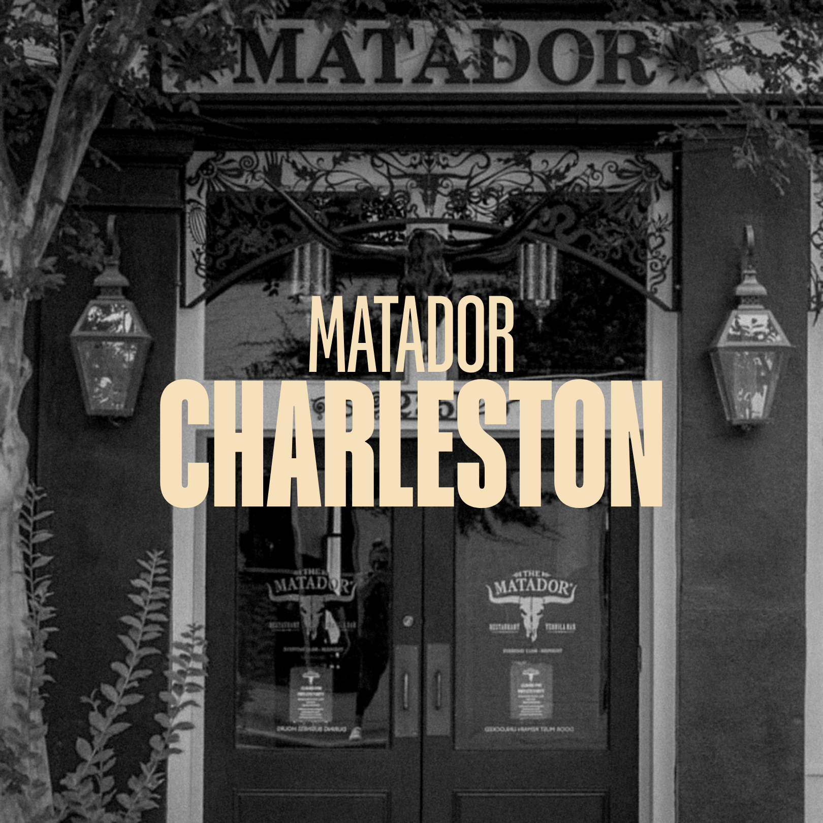 Black and white photo of the entrance to a restaurant called "Matador" with large signage and decorative lanterns, surrounded by trees and foliage.