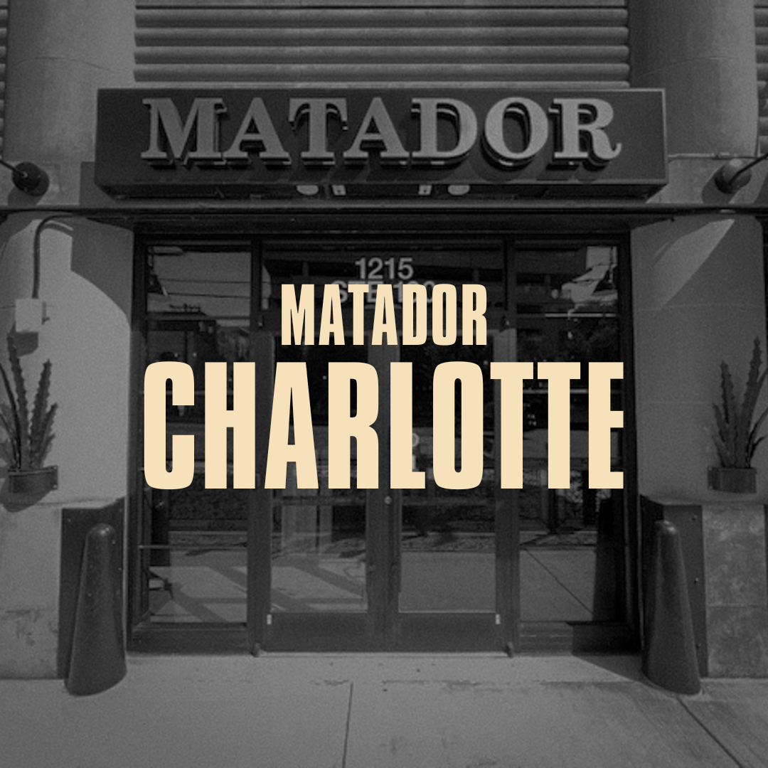 storefront with a sign for Matador Charlotte, 1215, with two potted plants on either side of the entrance.