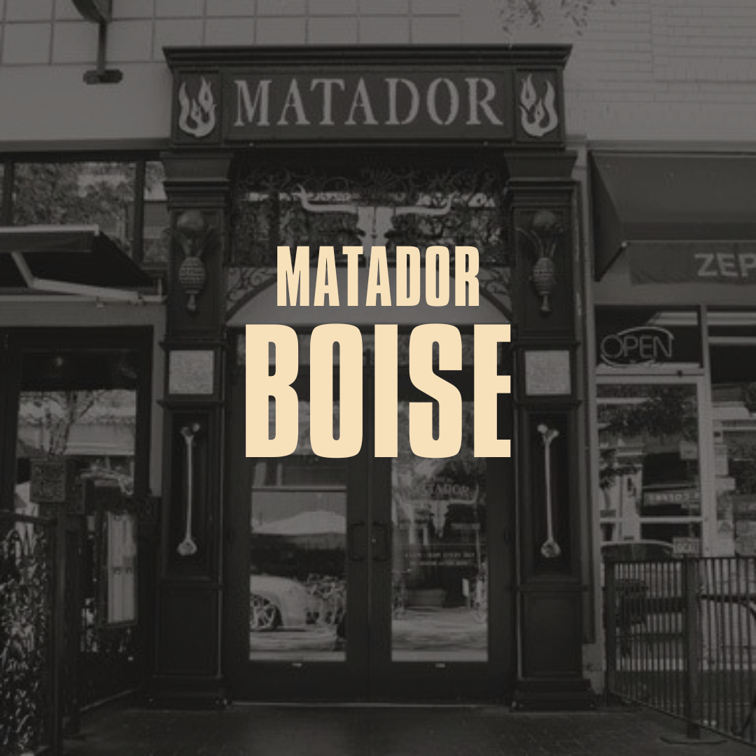 Black and white photo of the entrance to a restaurant named Matador Boise with a large sign above the door that says 'MATADOR' and decorative elements with flames. The words 'MATADOR BOISE' are overlaid prominently.