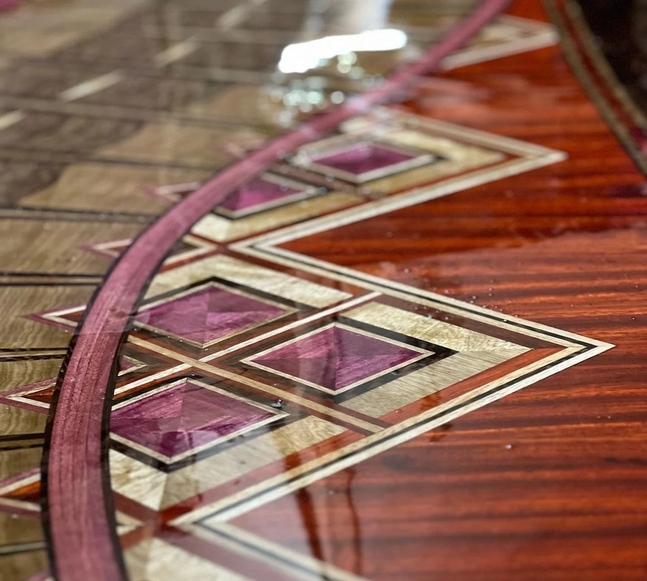 Close-up of a detailed inlay wood veneer tabletop with geometric patterns and a curved pink border.