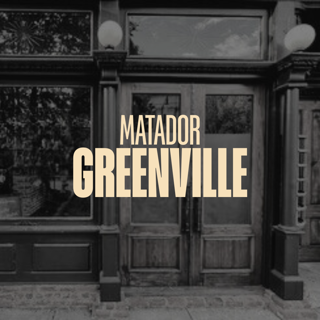 Black and white photo of a building with large windows and wooden door, with the text 'Matador Greenville' overlaid in bold font.