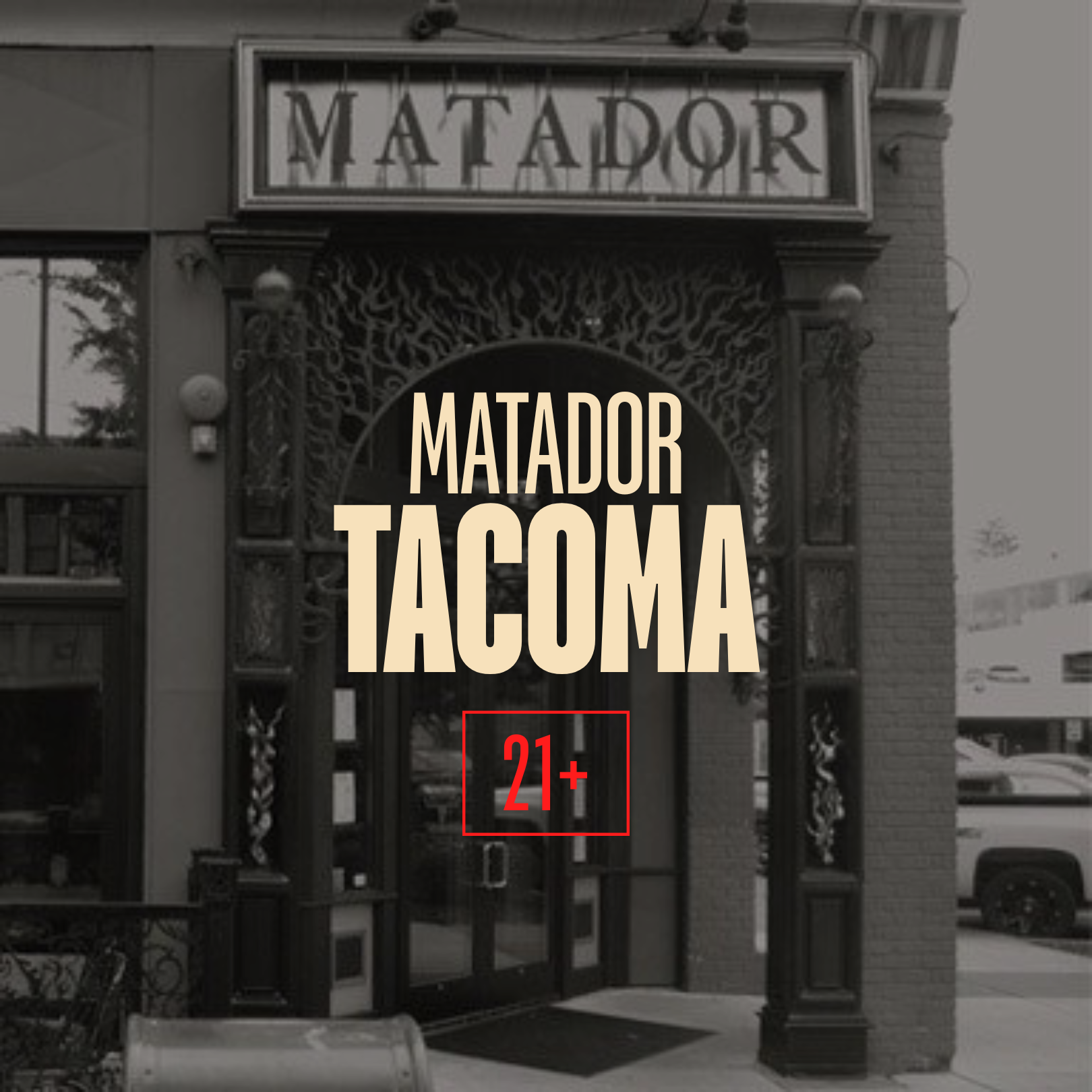 The exterior of a restaurant called Matador Tacoma with its sign visible at the entrance, featuring decorative black metalwork and greenery around the entrance. The photo is in black and white.