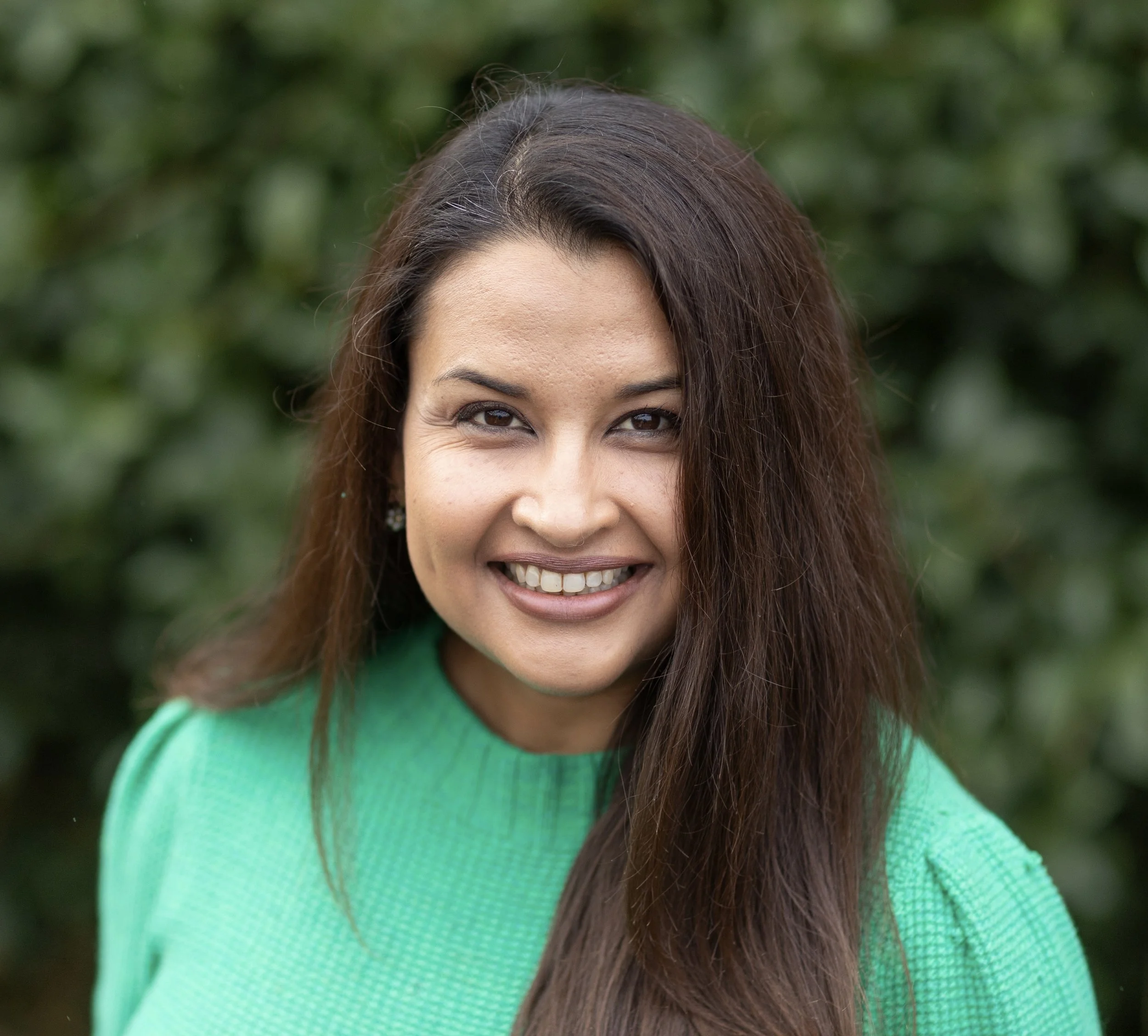 a picture of dr. bhattacharjee smiling in a green sweater in front of a background of green plants