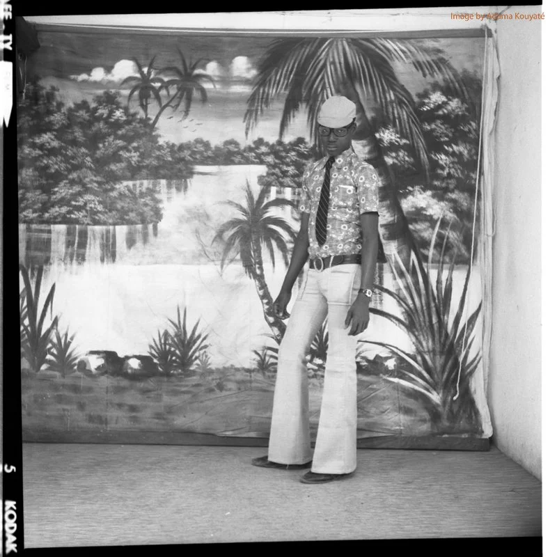 a man with a hat and a pair of glasses, he is dressed in shirt over old-fashioned pants, October 1973 Ségu, Mali, © adama kouyaté.