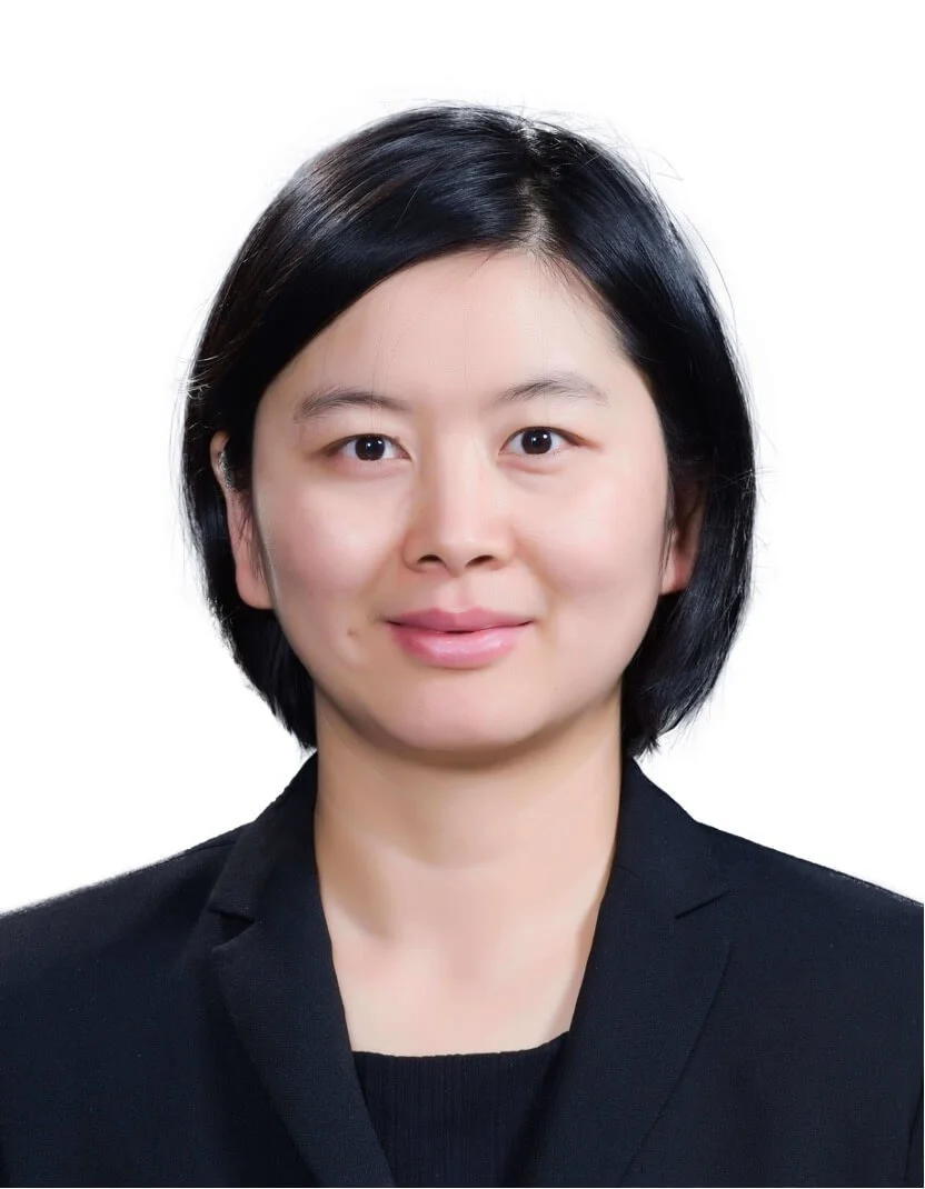 Portrait of a woman with short black hair, wearing a black blazer, smiling softly against a white background.