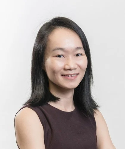 A woman with straight black hair wearing a sleeveless dark purple top, smiling at the camera against a plain white background.