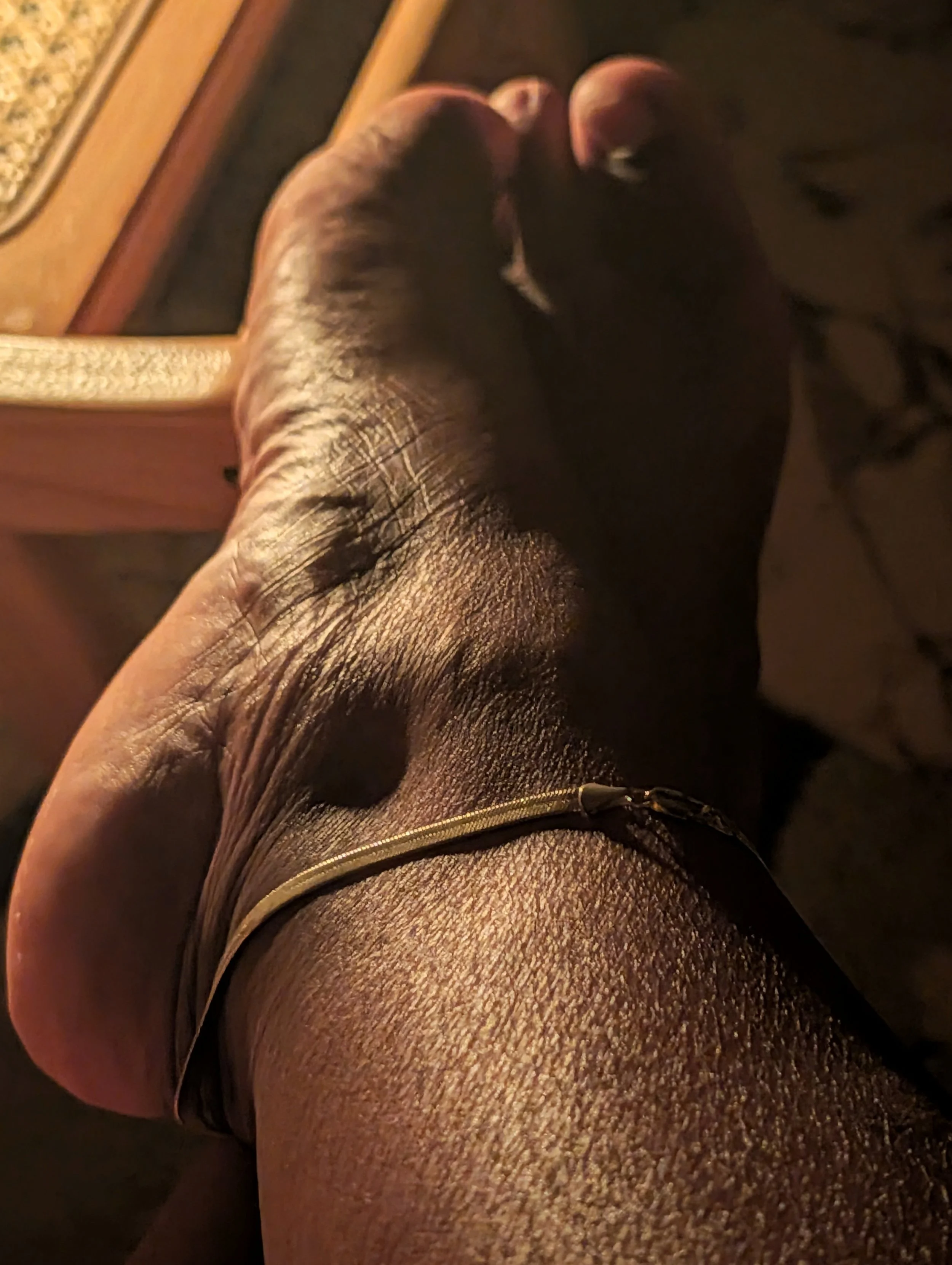 Black person's feet, posing on the edge of a footstool, lit by candlelight. soft, romantic, feet lovers rejoice. 