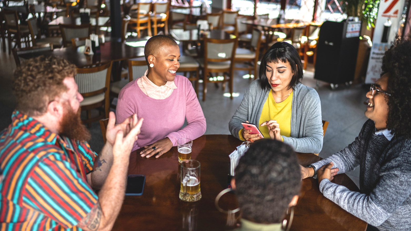 Five people sitting around a table, enjoying drinks and conversation in a casual restaurant or cafe.