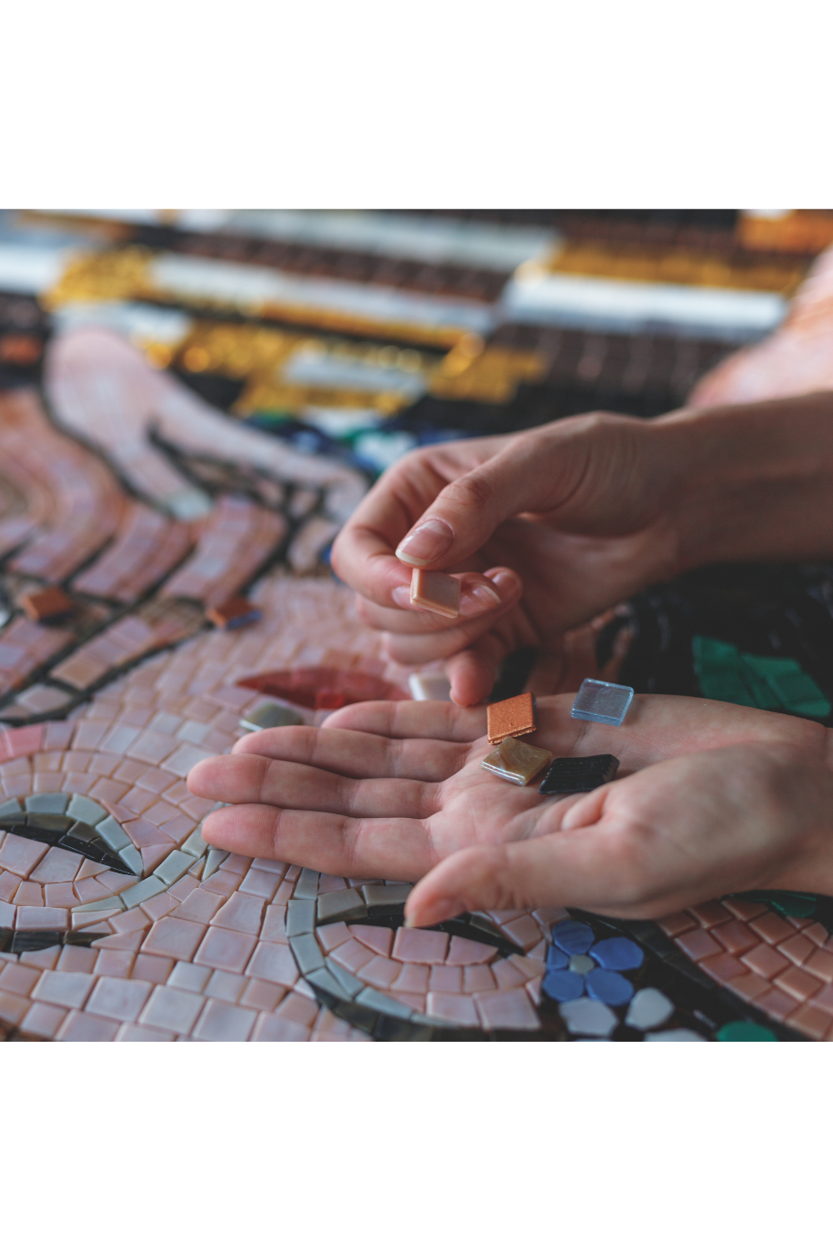 Hands placing small, colored ceramic tiles onto a mosaic art piece.