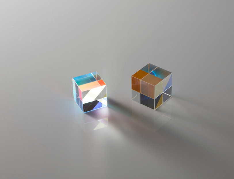 Two small glass cubes with iridescent surfaces on a reflective surface